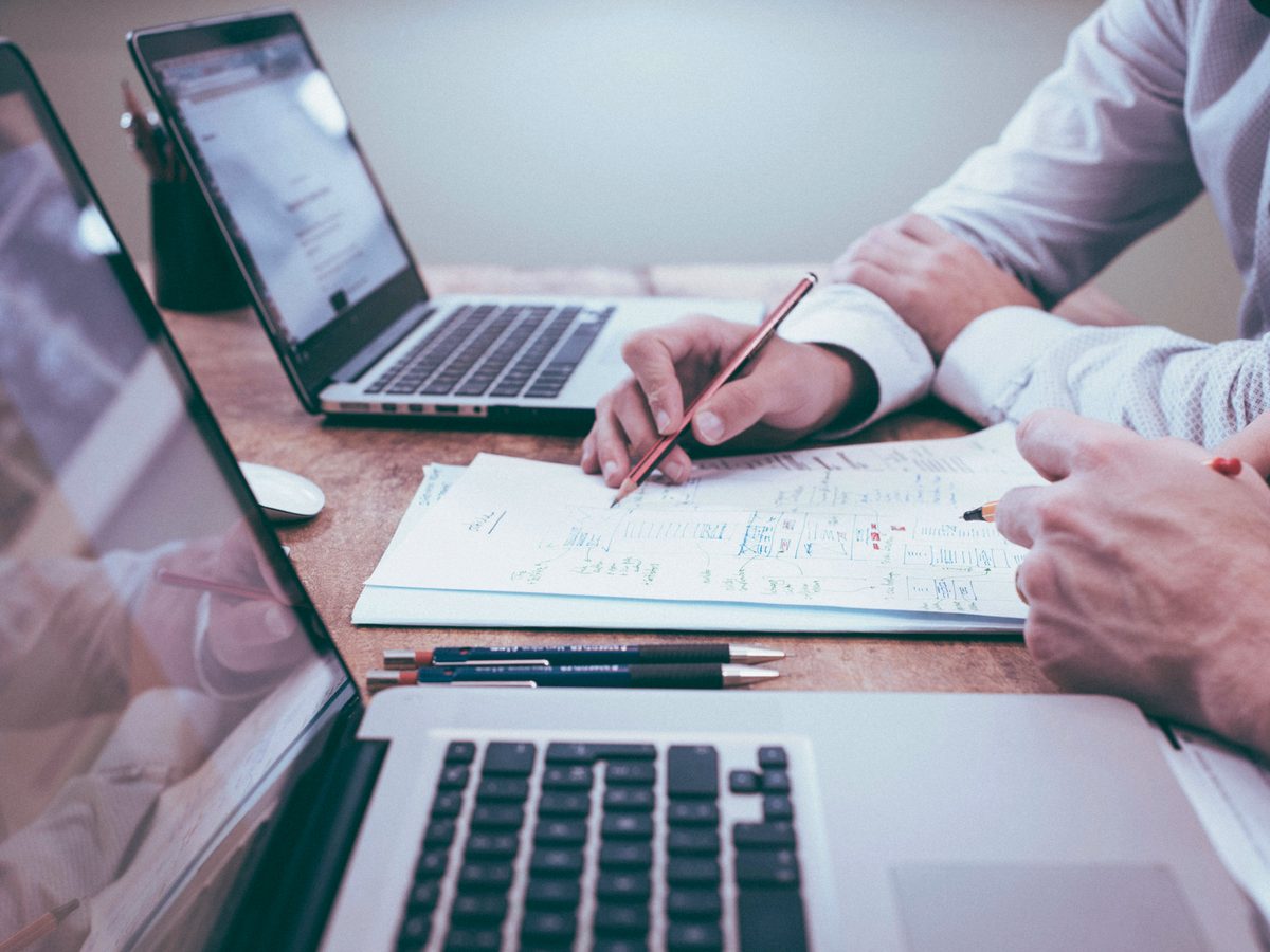 Dois profissionais analisando relatórios contábeis com laptops sobre a mesa